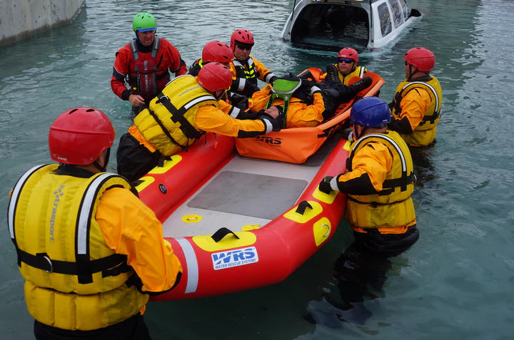 Group of people in yellow vests and red helmets around an inflatable raft in water.