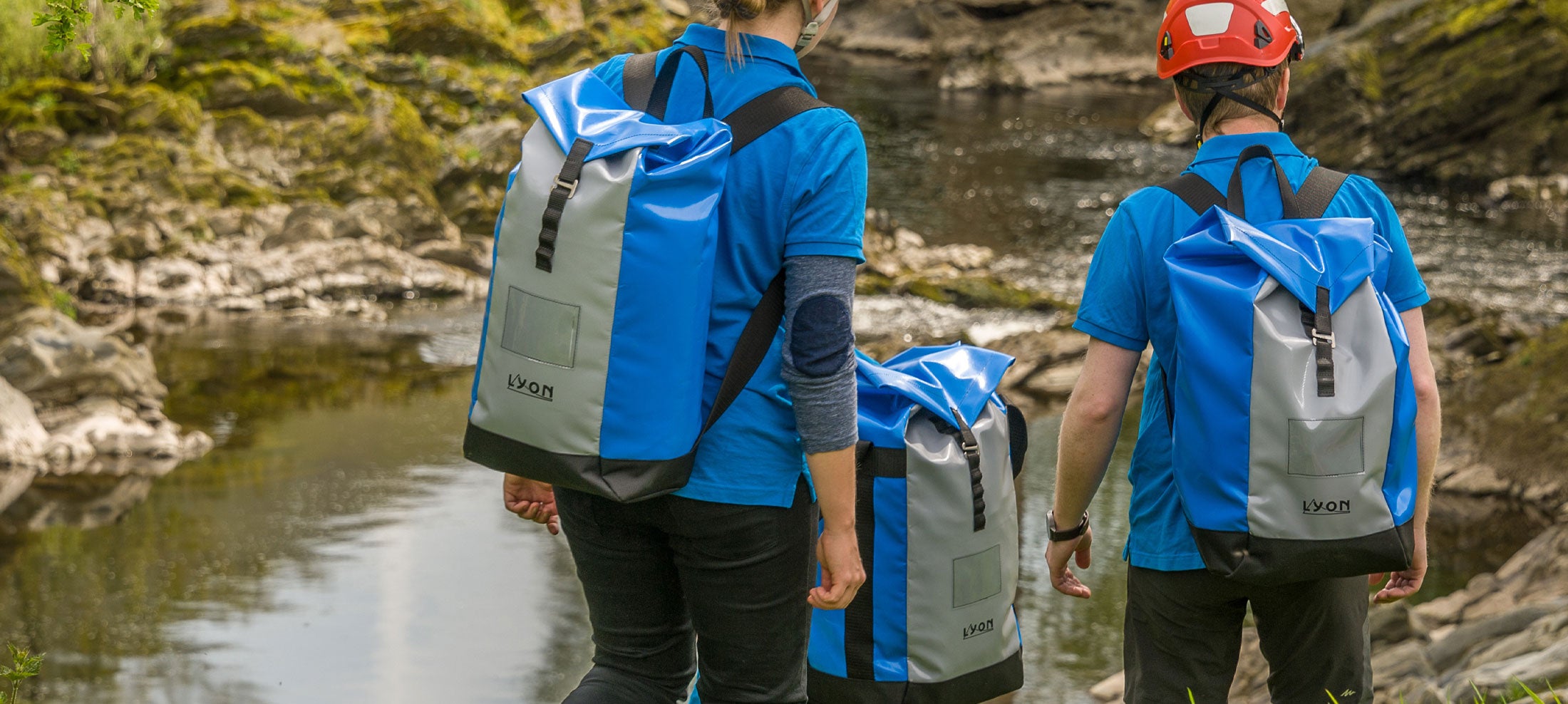 Two people with backpacks standing by a stream in a natural setting
