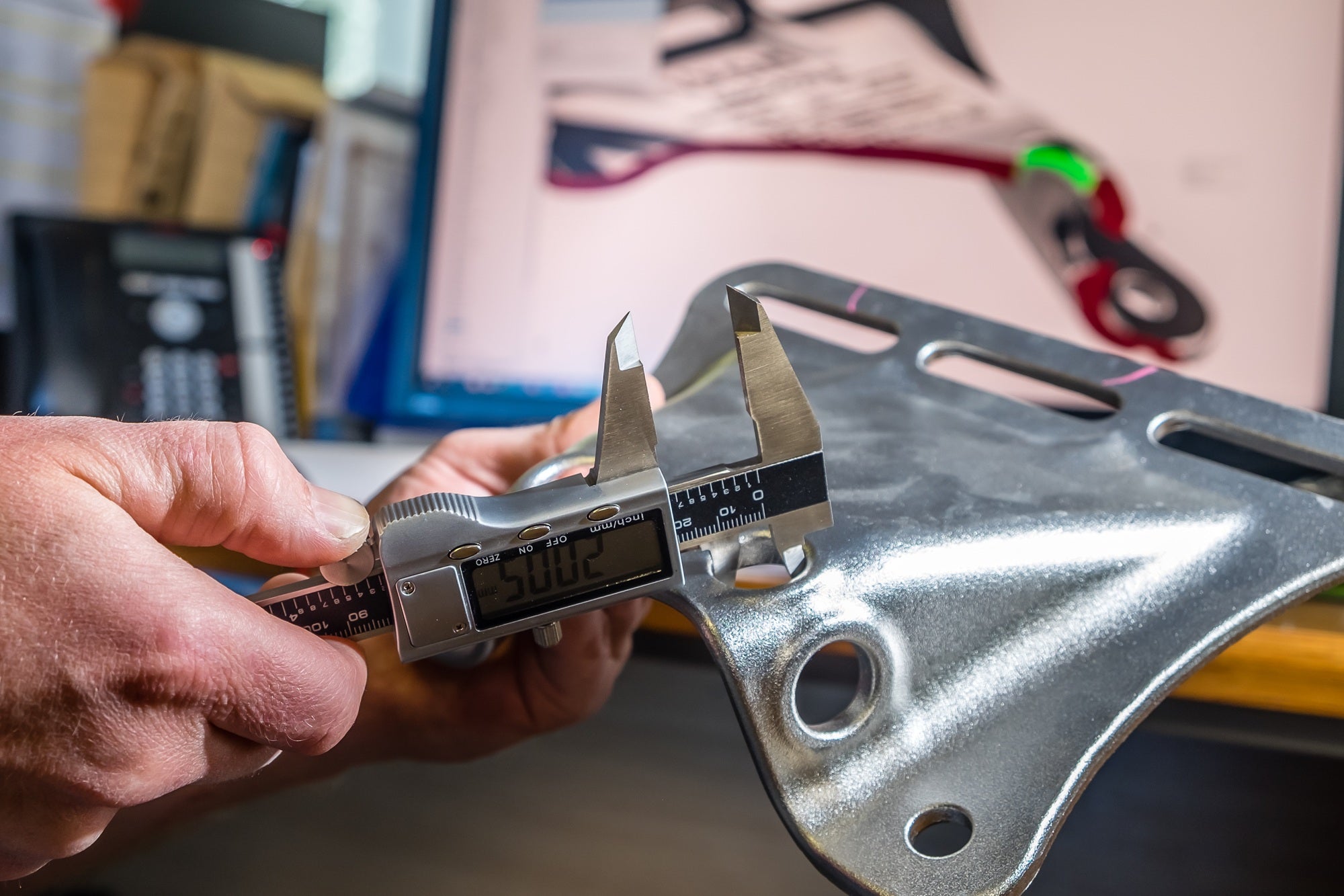 Person using a digital caliper to measure a metal object with a blurred workshop background
