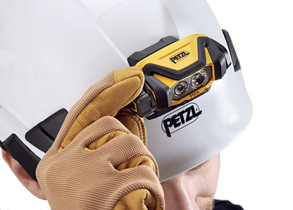 Person wearing a white helmet with a Petzl headlamp and brown gloves on a white background