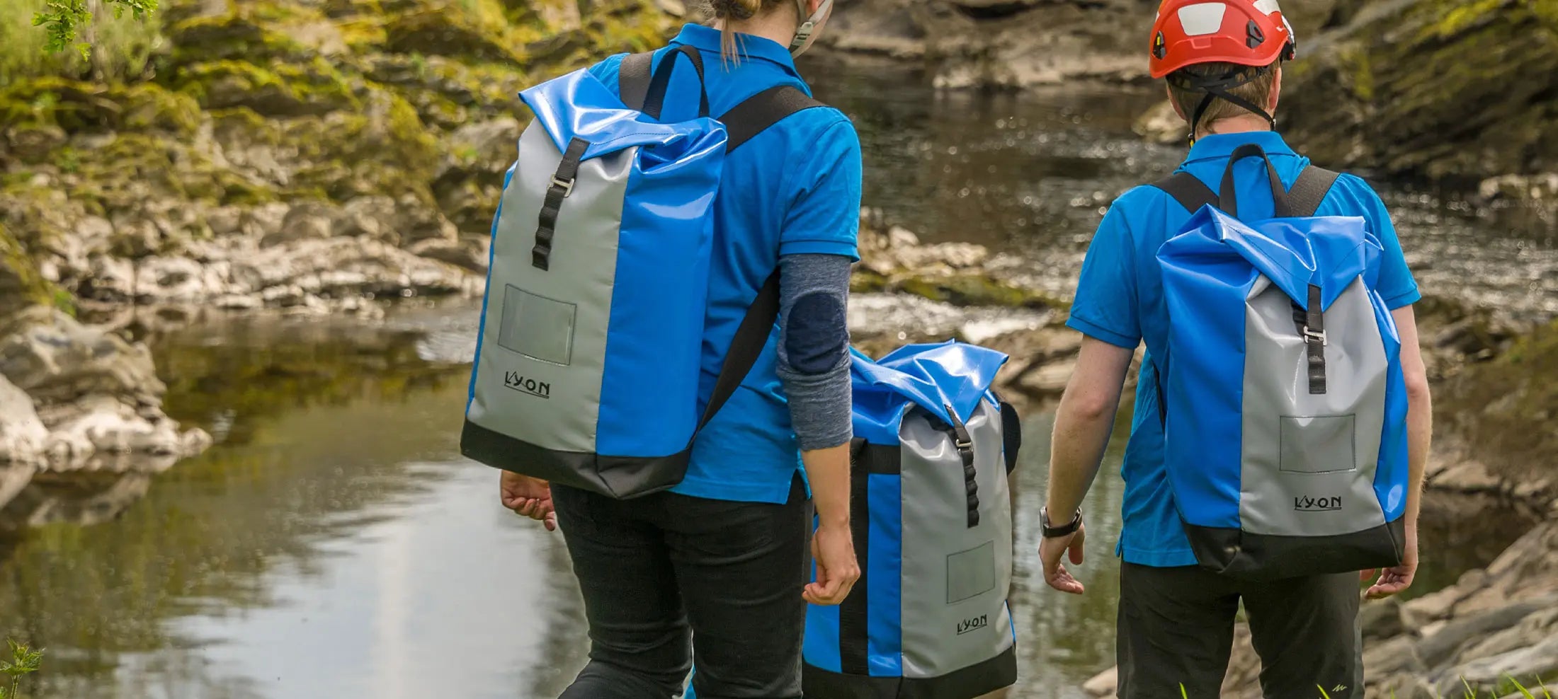 Two people with backpacks standing near a body of water in a natural setting