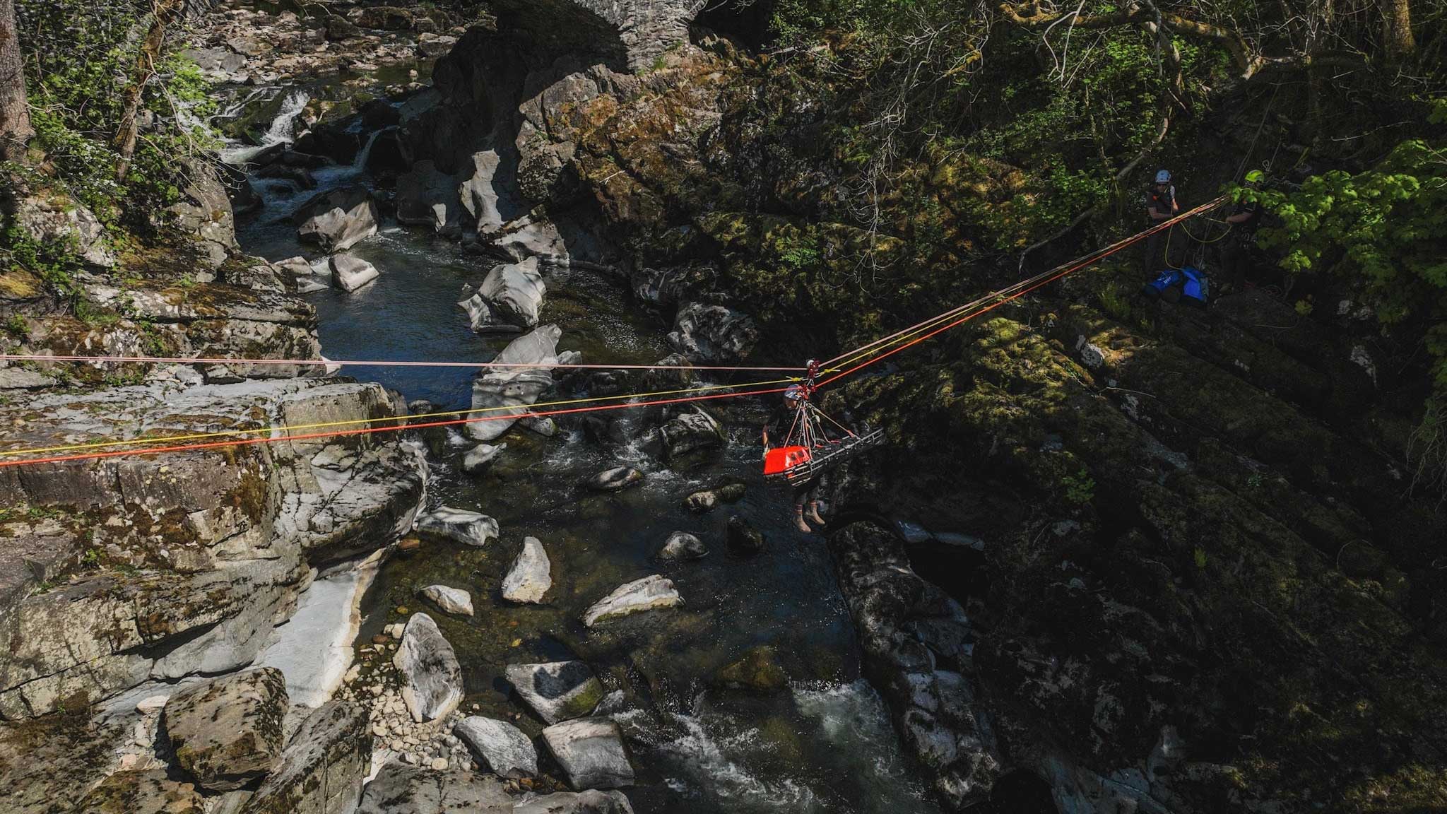 Person on a rope bridge over a rocky gorge with greenery