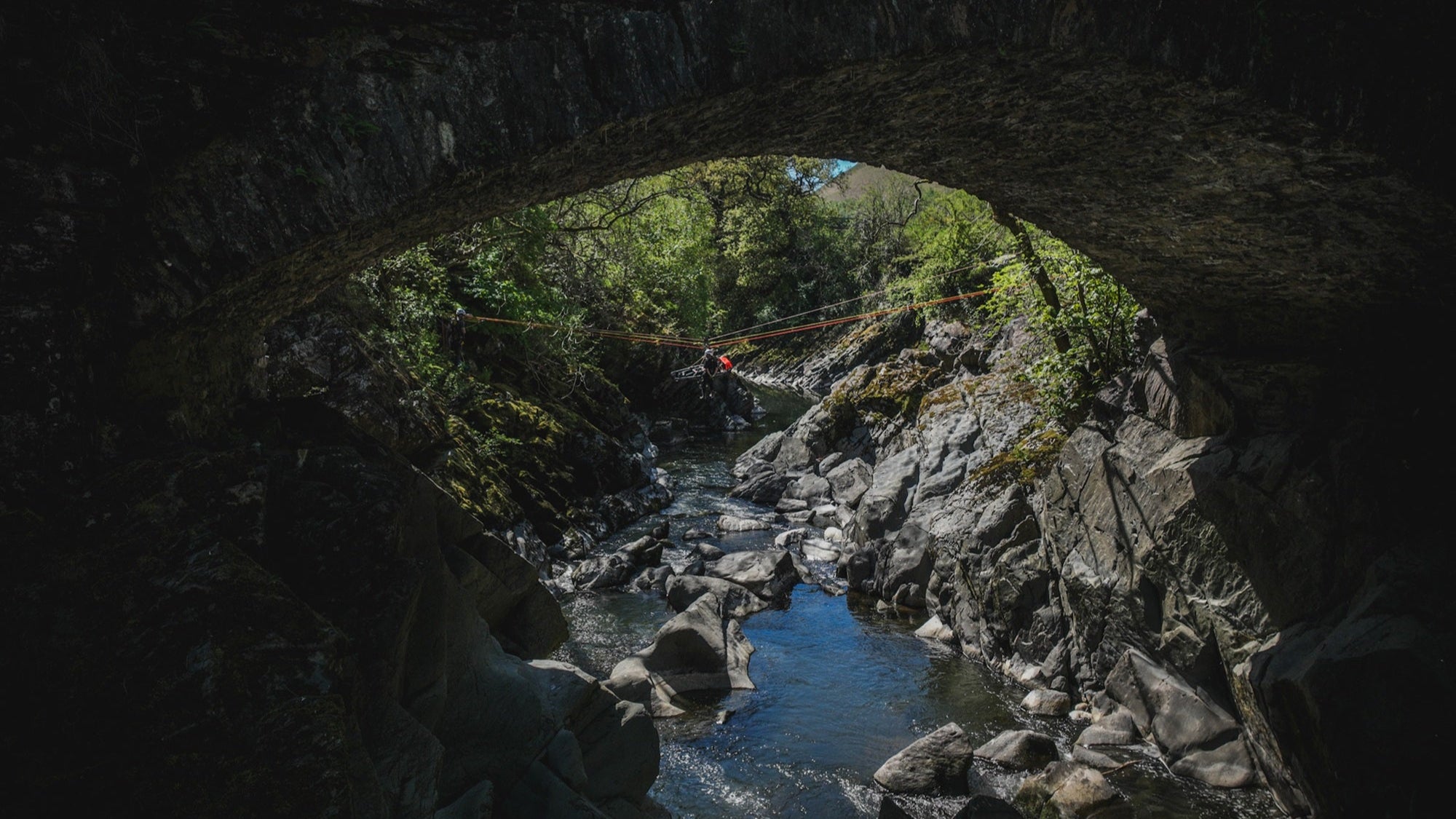 View of a river through a stone archway with greenery on either side.