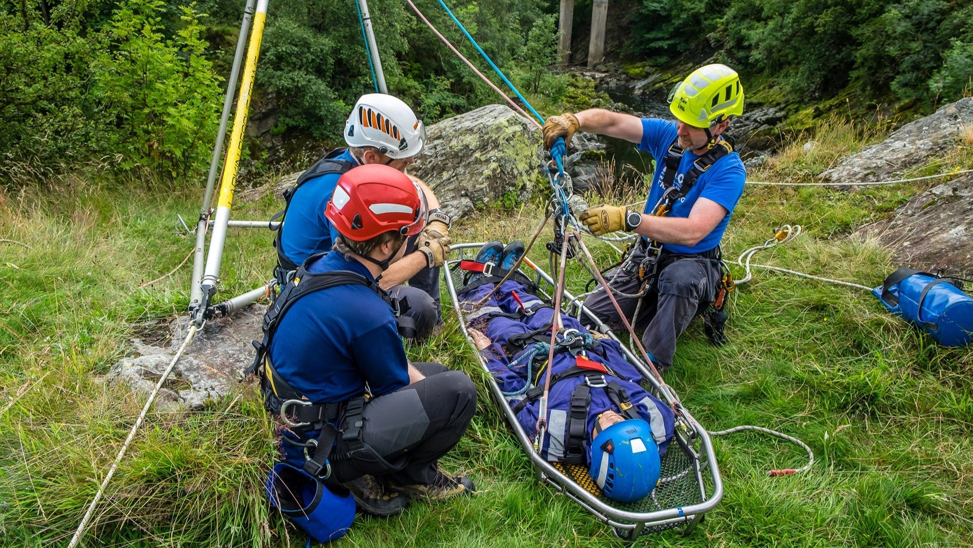 Three rescue workers with equipment on a stretcher in a forest setting